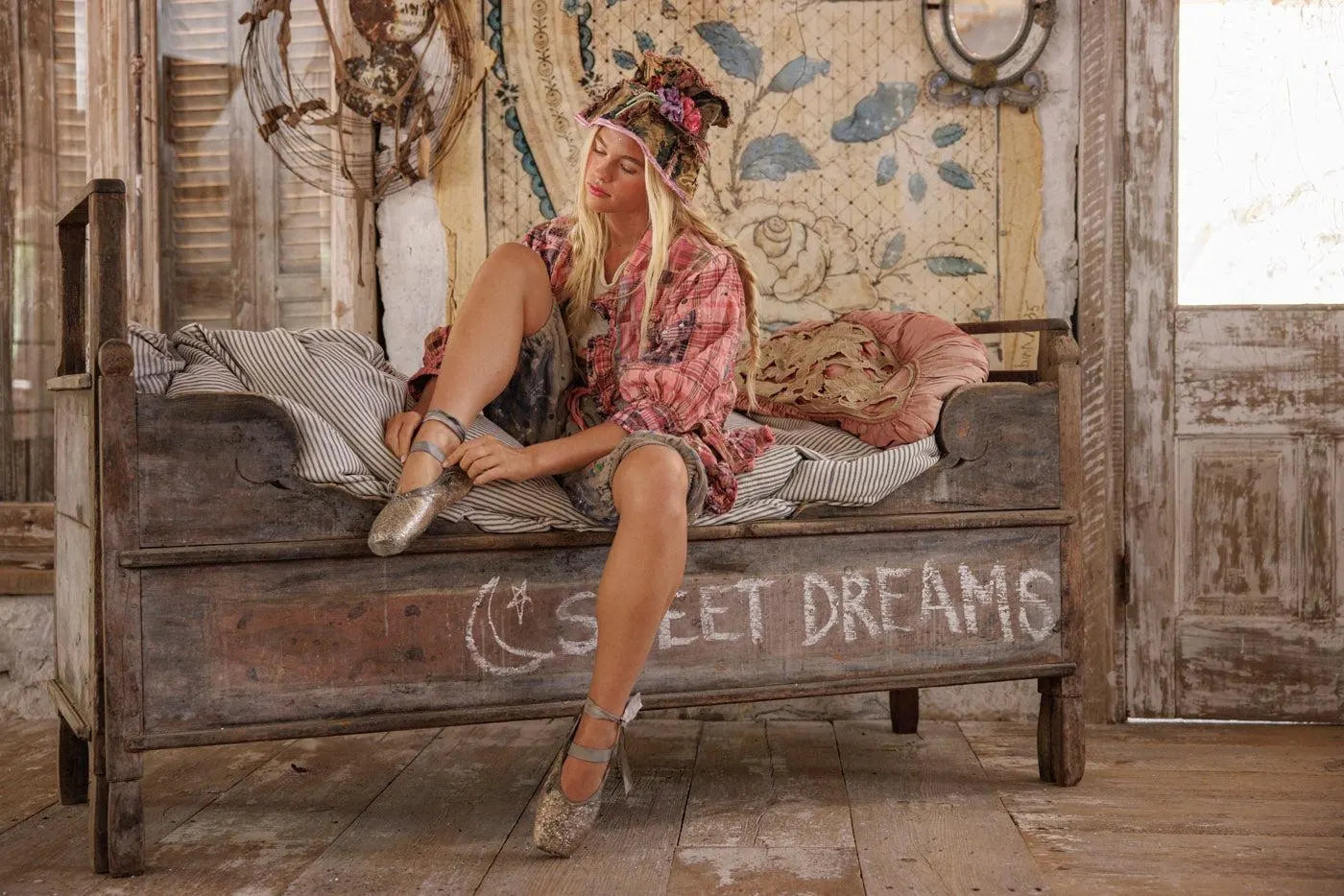 Woman in Magnolia Pearl artisan vintage clothing with whimsical designs sitting on rustic daybed