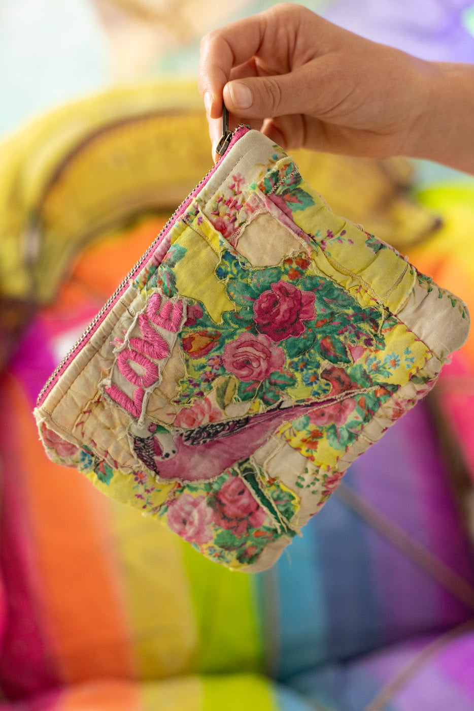 Colorful floral-patterned fabric zipper bag and or makeup bag  held by a hand against a blurred background
