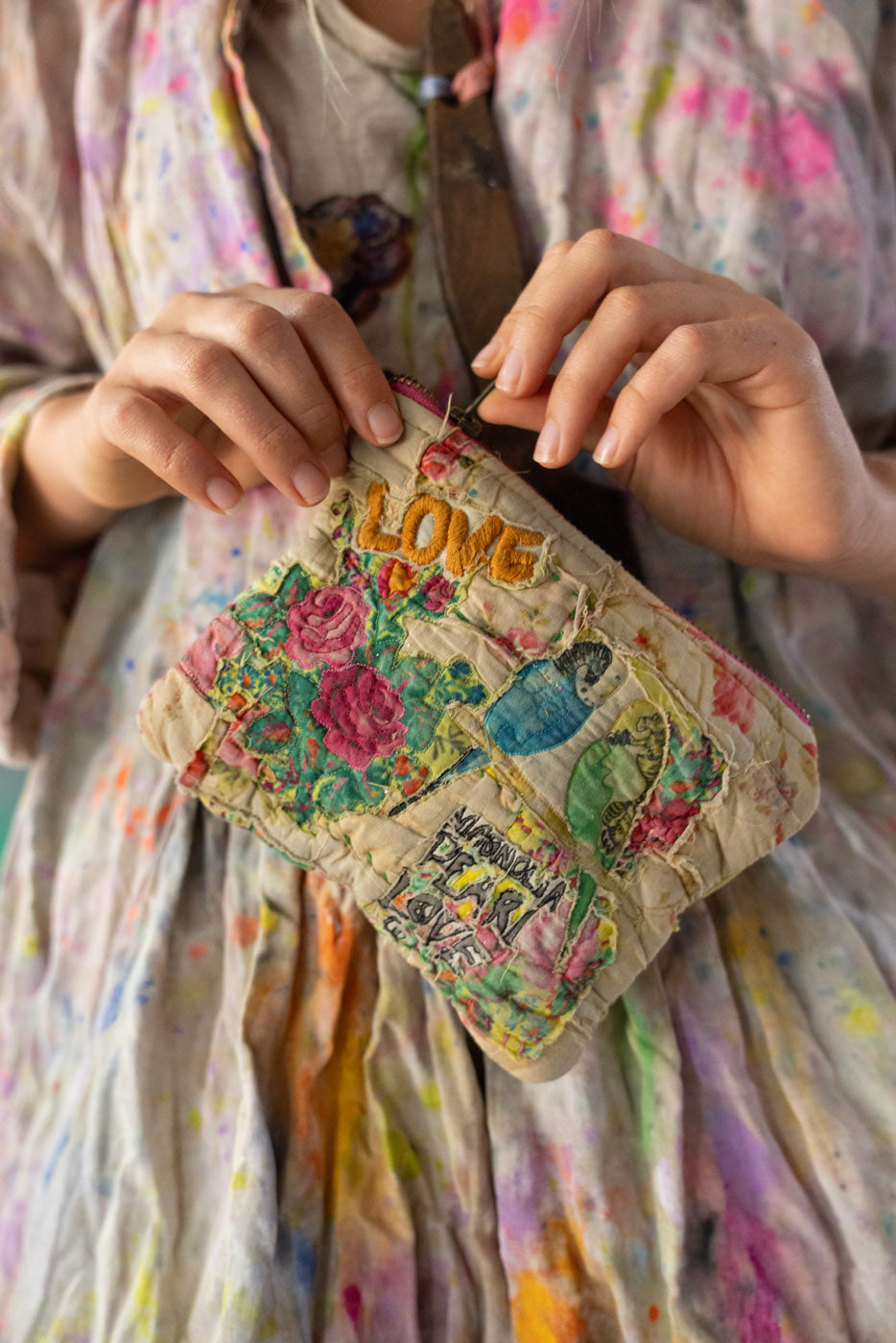 Person holding a small, embroidered bag / makeup bag / patchwork bag with floral designs and the word 'LOVE'.