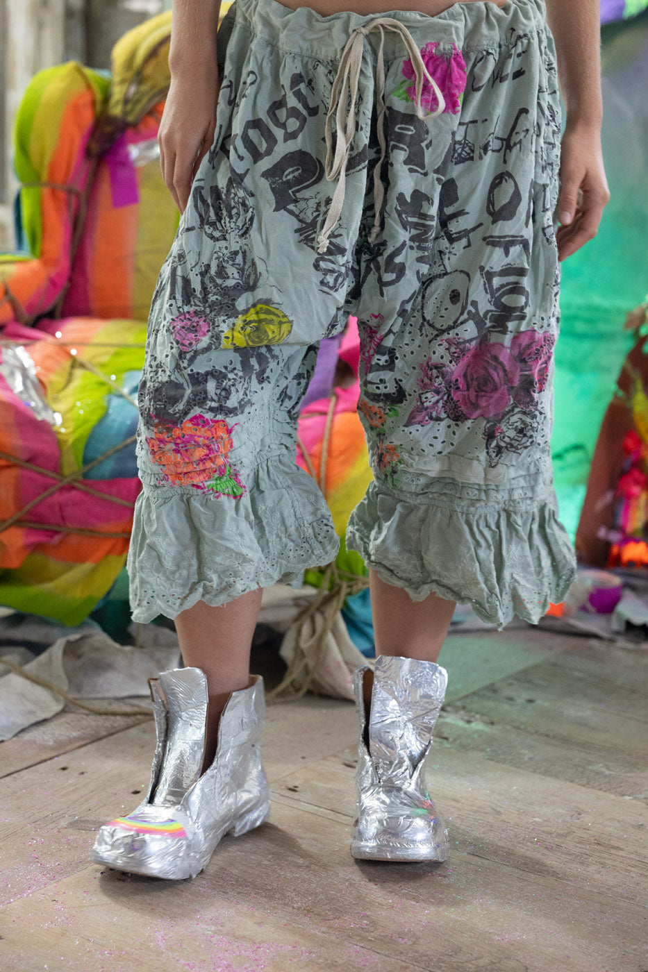 Person wearing colorful, patterned shorts with metallic shoes on a vibrant background