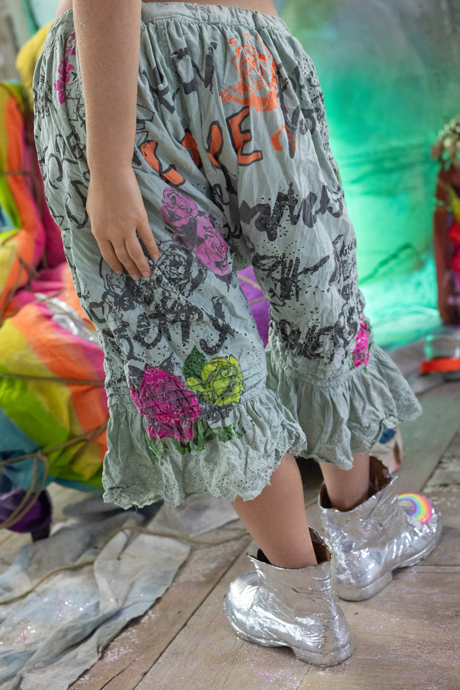 Person wearing a colorful shorts with text and floral patterns, standing on a stone floor with a blurred background.