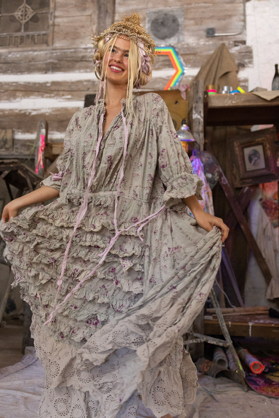 Model wearing Magnolia Pearl floral ruffle dress with lace hem in rustic studio, soft lilac print and flowing silhouette.