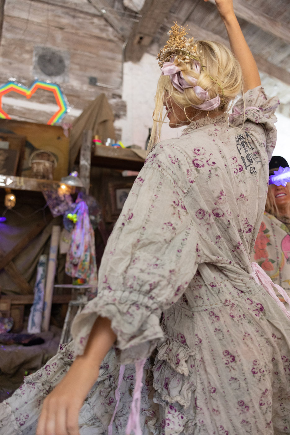 Person in a vintage floral dress with decorative headpiece  in a rustic indoor setting.