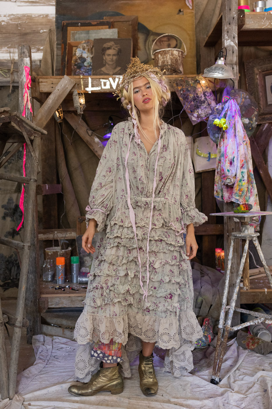 Person wearing a floral dress and headpiece in a rustic indoor setting with wooden beams and various items. Logger look.