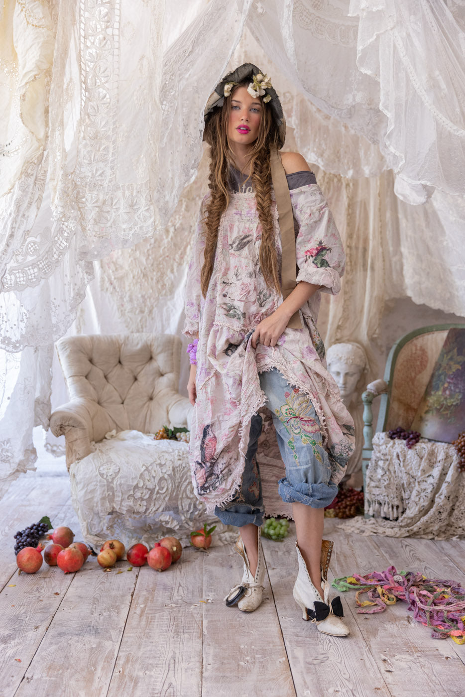 Magnolia Pearl model in whimsical vintage artisan dress and floral bonnet, lace backdrop, rustic setting