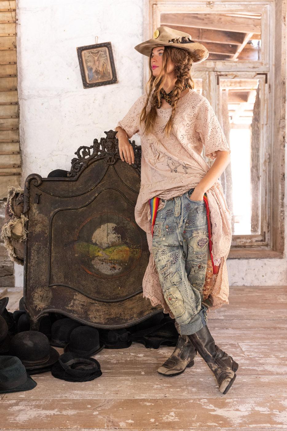 Woman in Magnolia Pearl vintage artisan lace dress, patched jeans, and rustic hat in shabby chic room