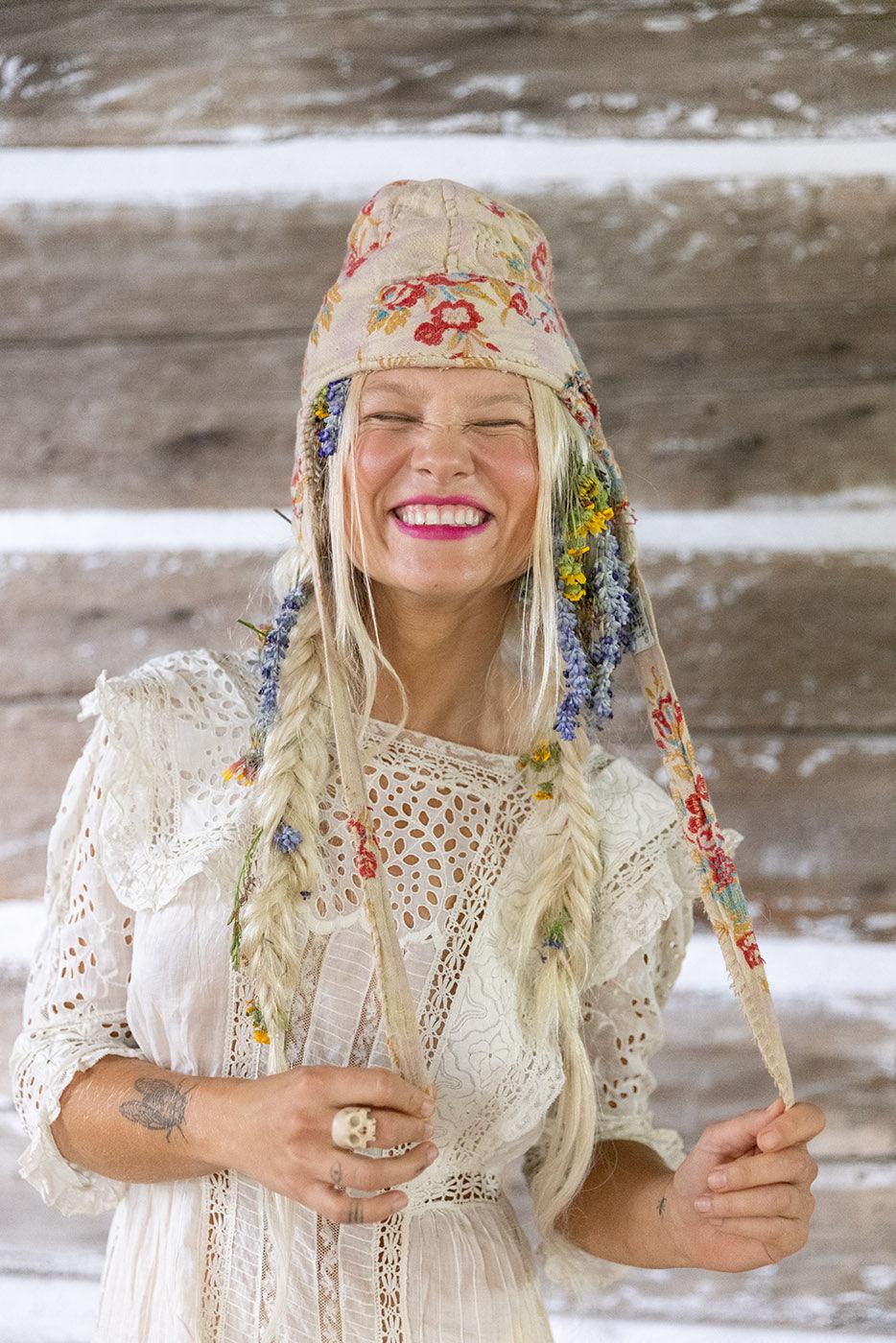 Smiling woman in Magnolia Pearl artisan floral hat and vintage lace dress, whimsical boho style