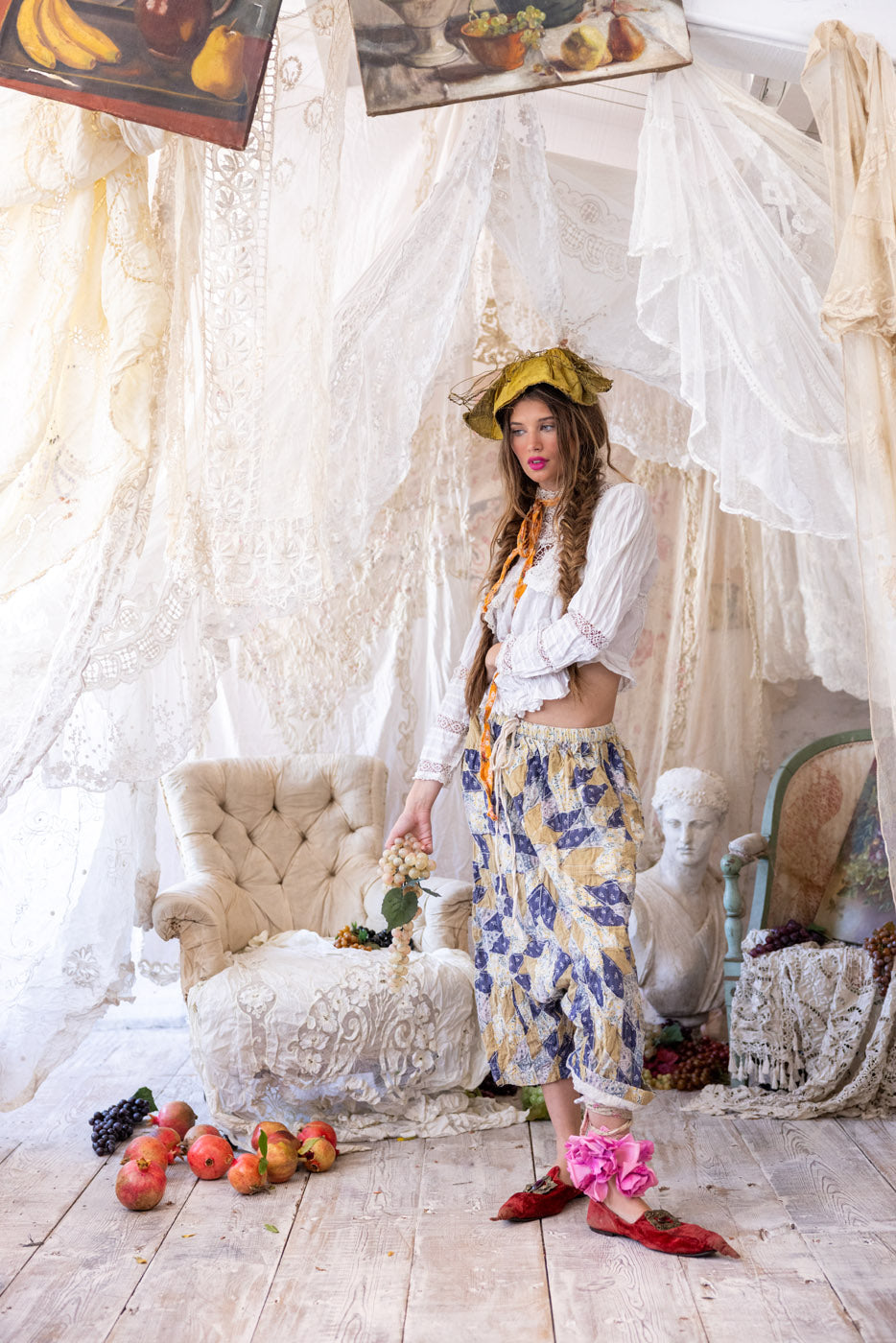 Magnolia Pearl model in vintage artisan clothing, whimsical lace setting, holding grapes, artful decor
