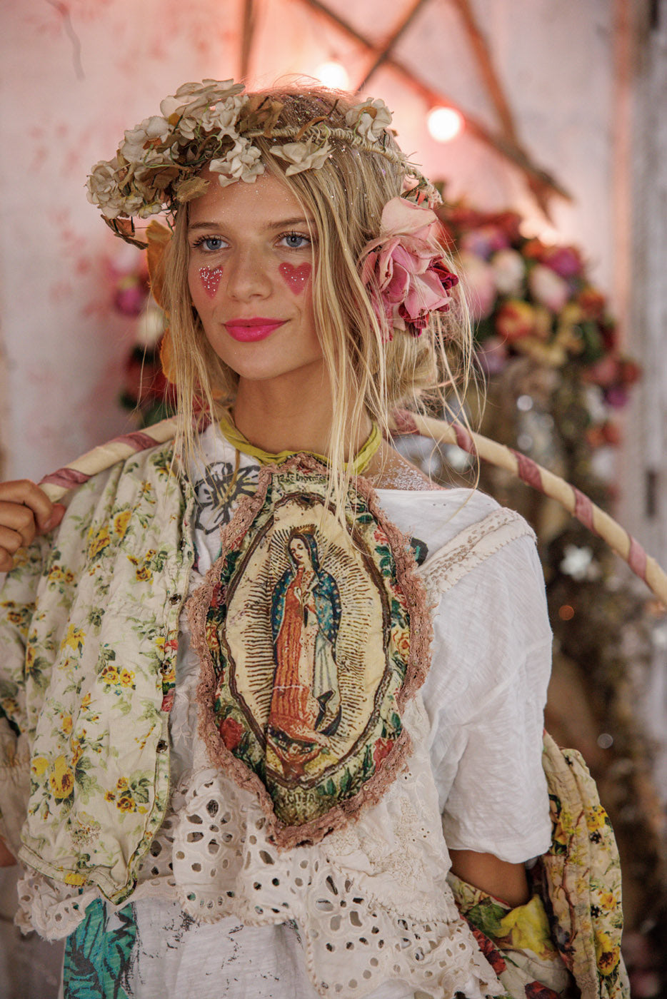 Woman in Magnolia Pearl artisan clothing with floral crown, vintage lace, and whimsical heart face paint