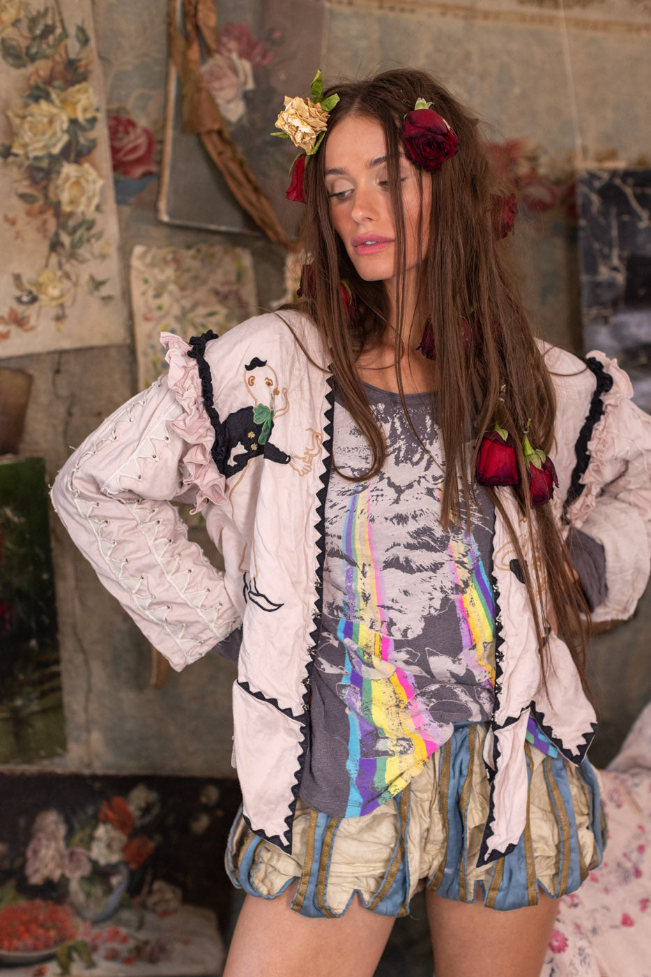 Woman in Magnolia Pearl vintage artisan jacket with whimsical rose accents, sitting on floral fabric.