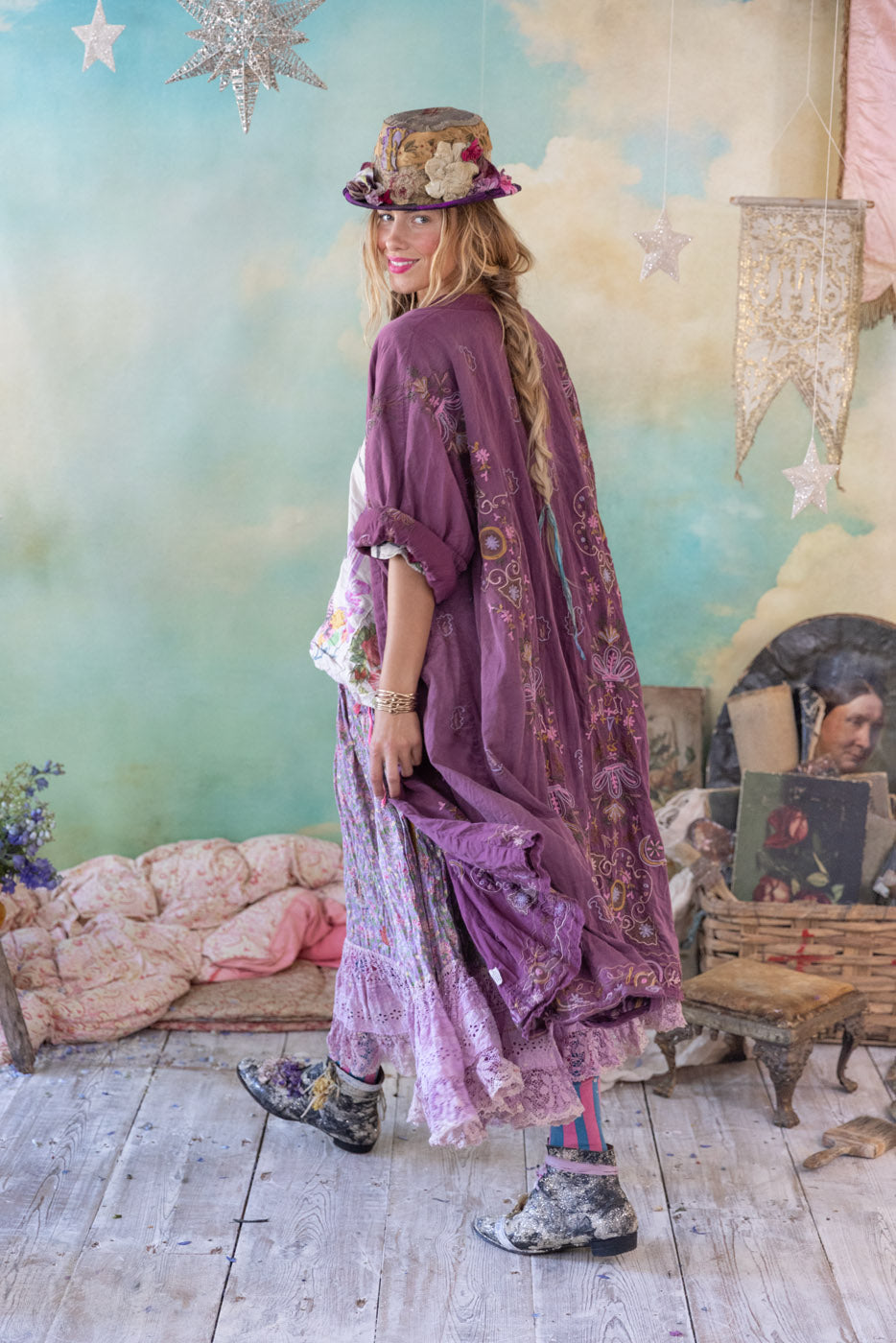 Bohemian woman in purple embroidered jacket, floral skirt, and hat in vintage room