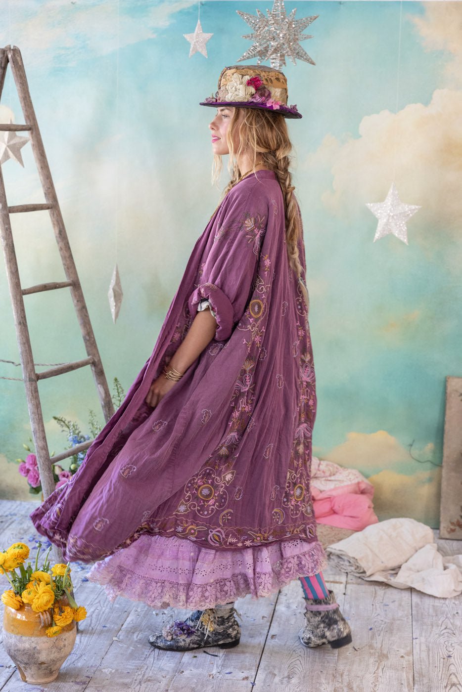 Bohemian woman in purple embroidered jacket, floral skirt, and hat in vintage room