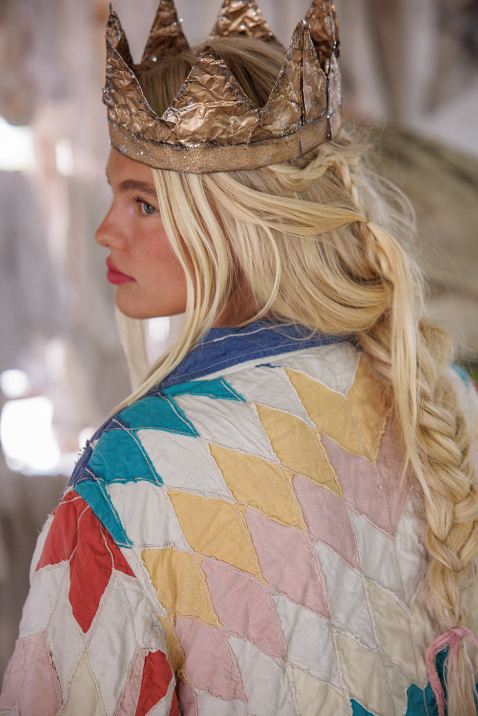 Woman in Magnolia Pearl vintage patchwork jacket and gold paper crown, whimsical artisan style