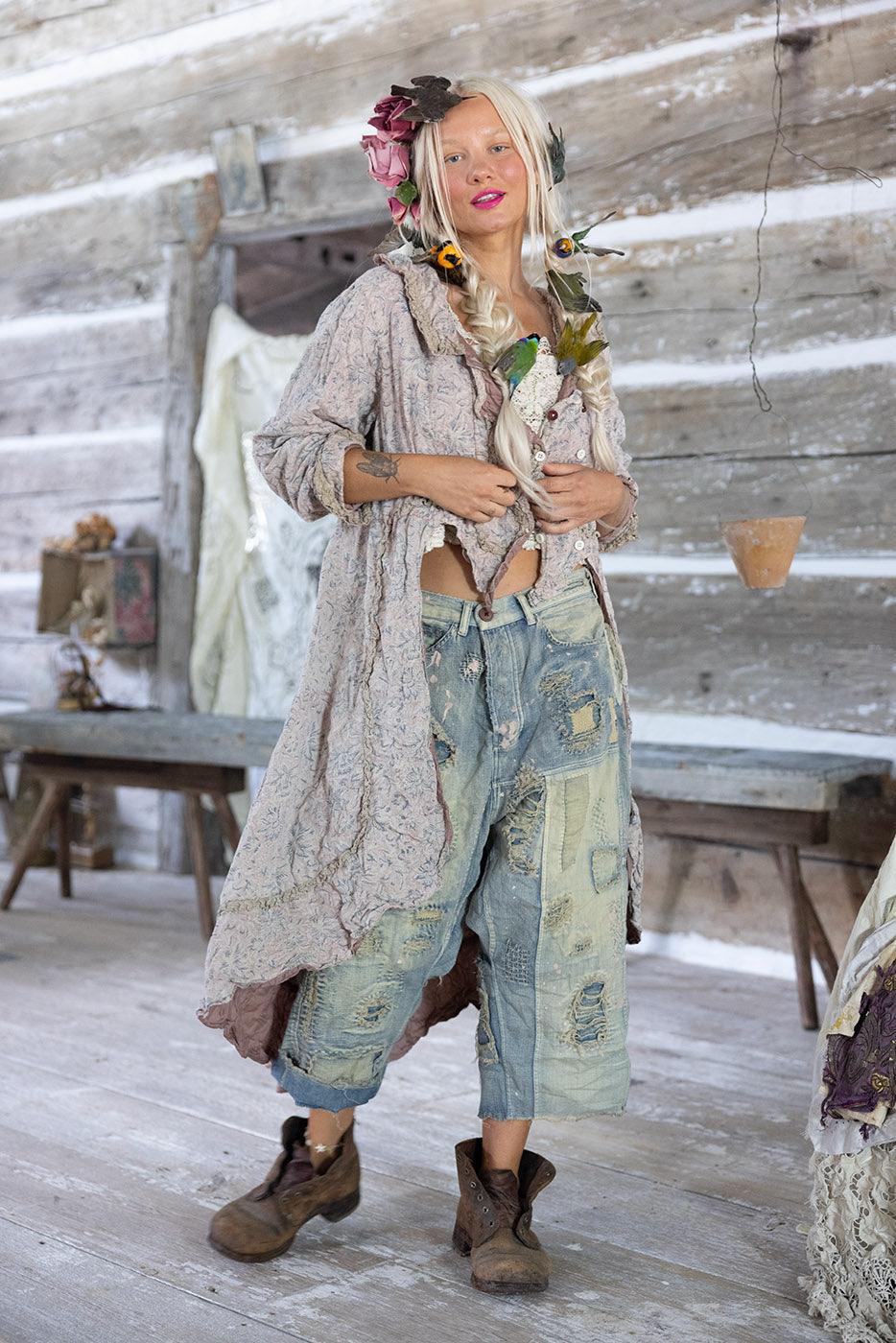 Woman in Magnolia Pearl artisan vintage-style jacket and distressed jeans with whimsical floral hair, rustic setting