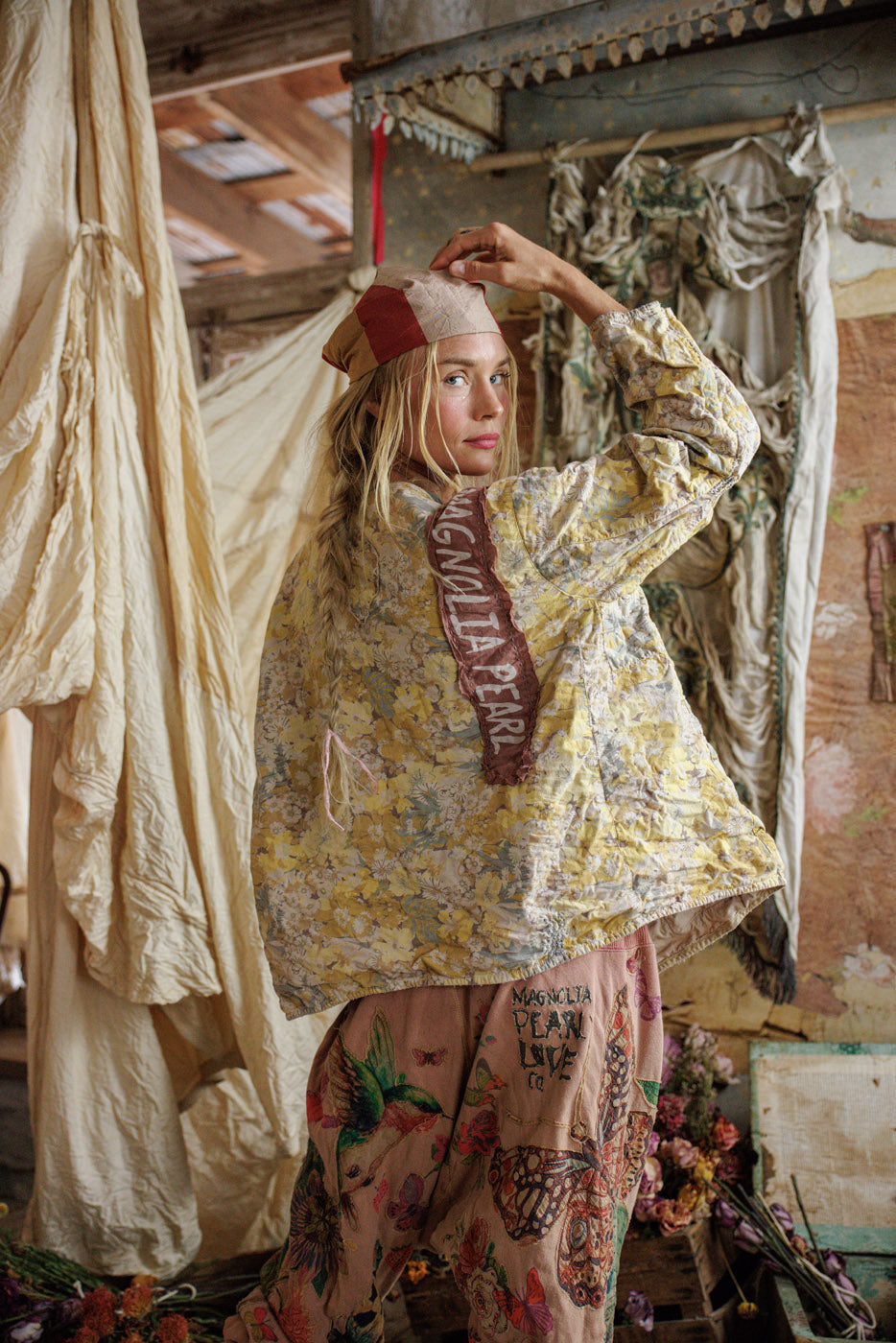 Woman in Magnolia Pearl artisan floral jacket and whimsical vintage pants, rustic vintage room