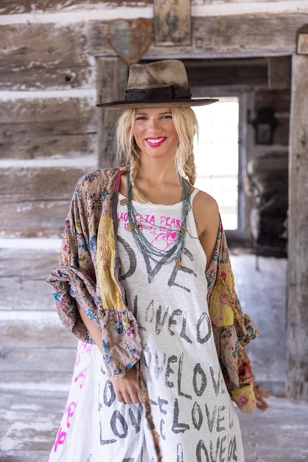 Woman in Magnolia Pearl vintage artisan dress with LOVE print, floral jacket, and hat in rustic setting