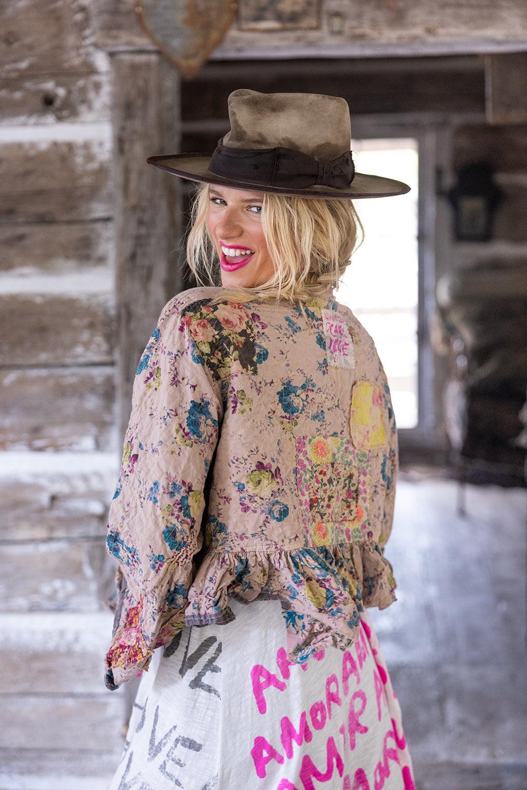 Woman in Magnolia Pearl artisan floral jacket and vintage hat, rustic background, whimsical style