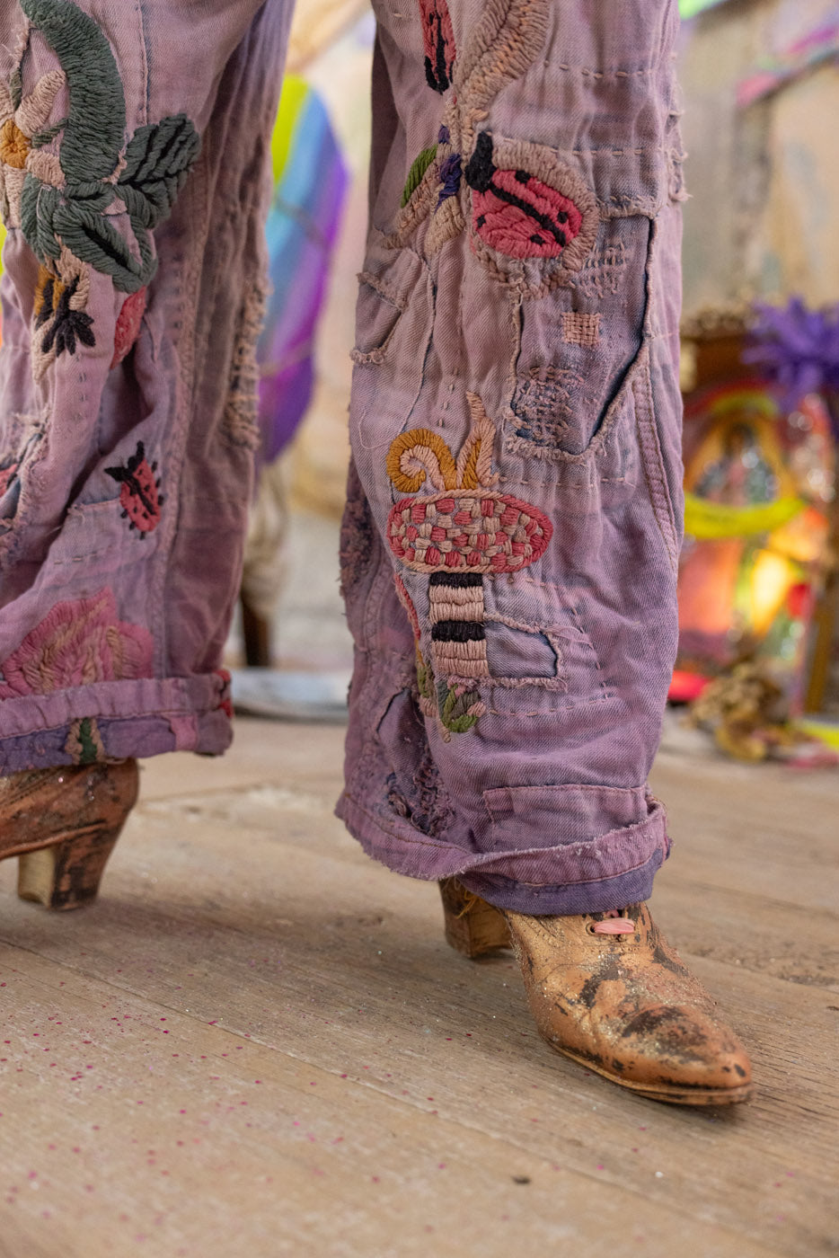 Purple embroidered magnolia pearl overalls with floral patterns worn by a person on a wooden floor.