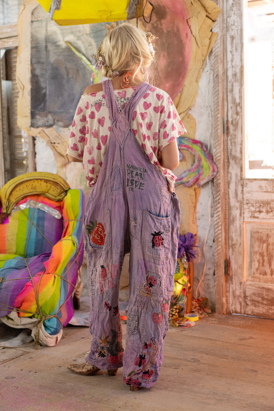 Person wearing a colorful overalls with floral patterns in a vibrant, artistic setting.