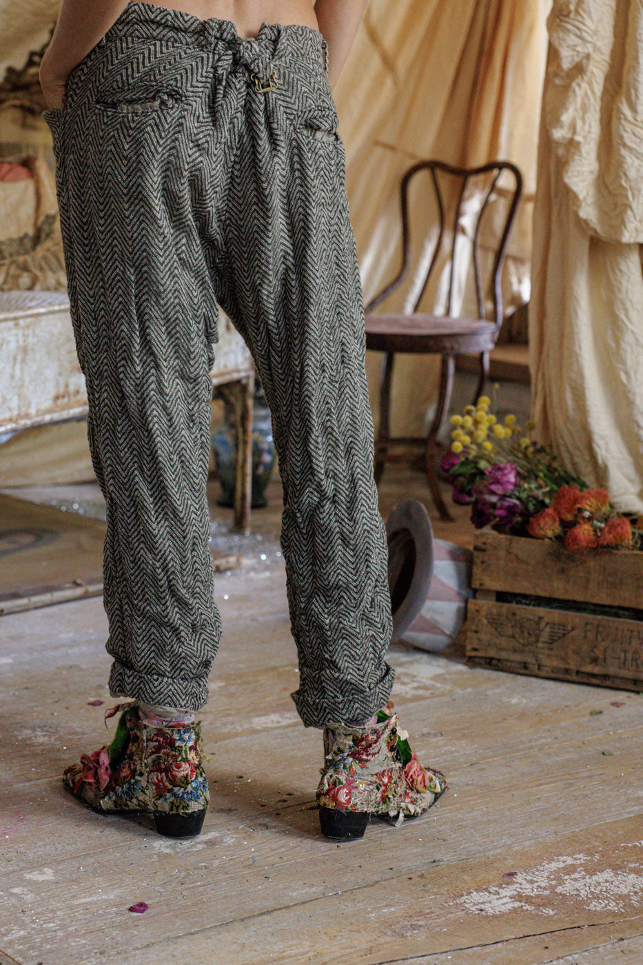 Person wearing herringbone pants and floral boots in a rustic vintage room with flowers