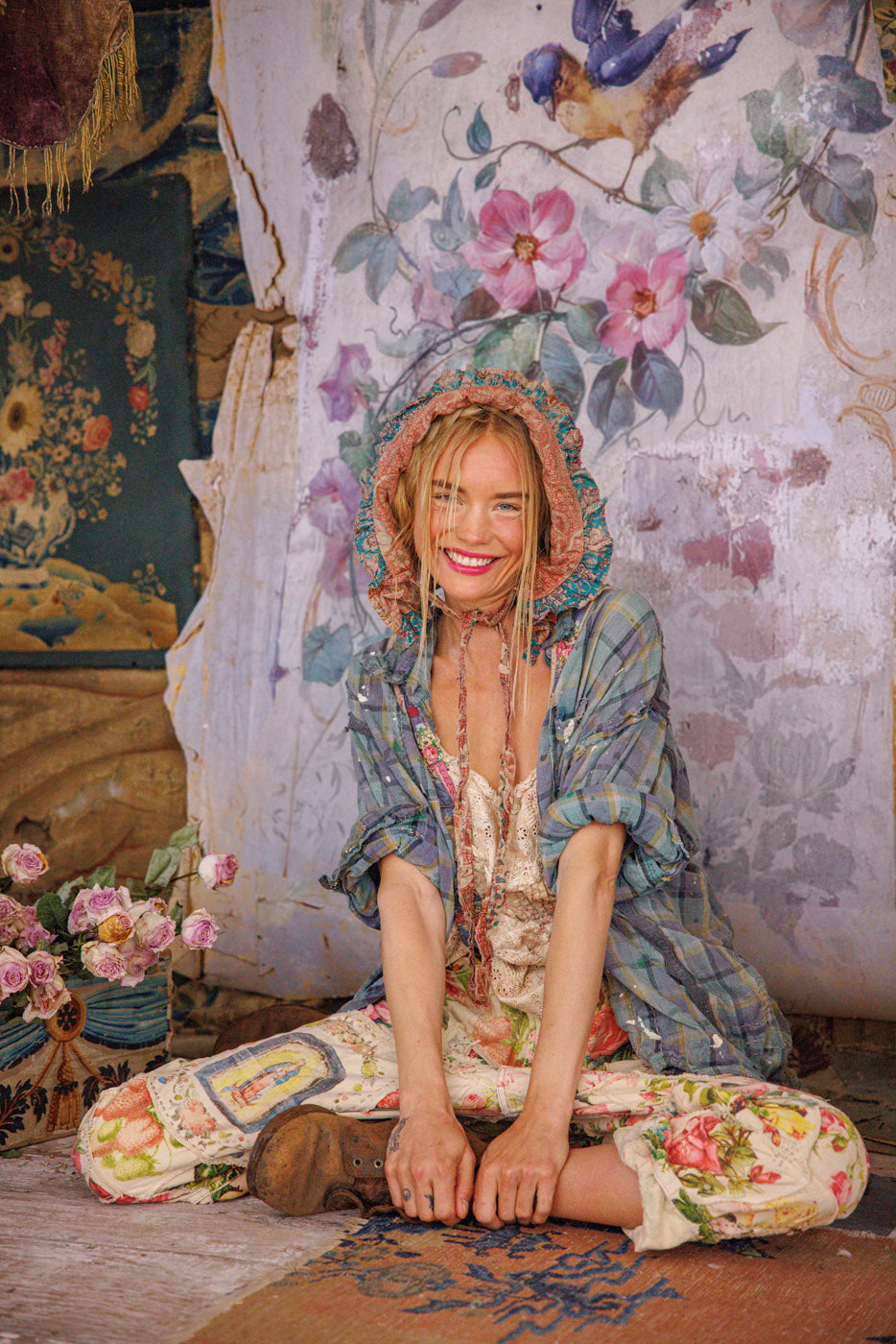 Woman in Magnolia Pearl artisan vintage floral pants and whimsical bonnet, sitting in boho setting