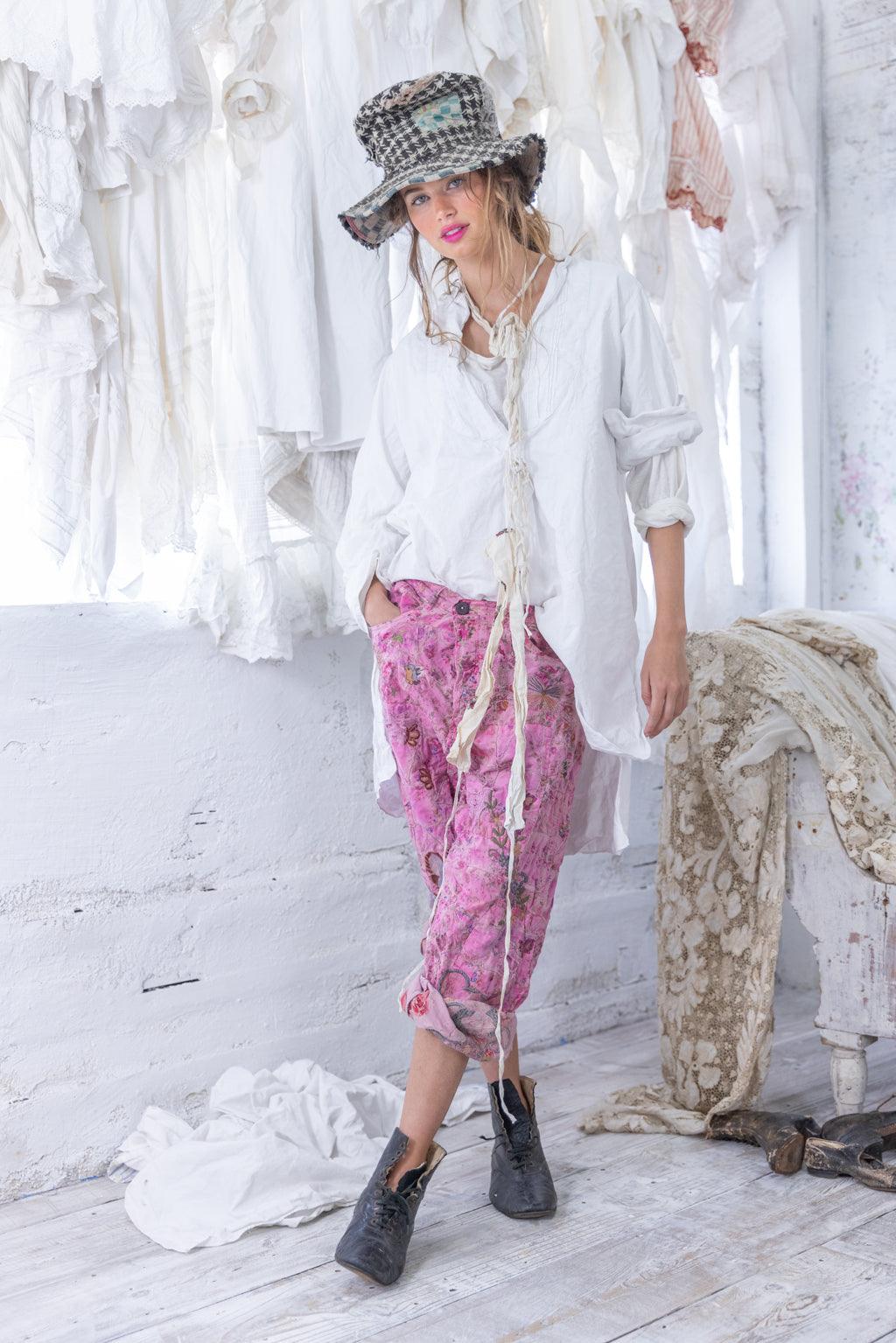 Woman in Magnolia Pearl pink artisan pants, white vintage blouse, whimsical hat, rustic setting