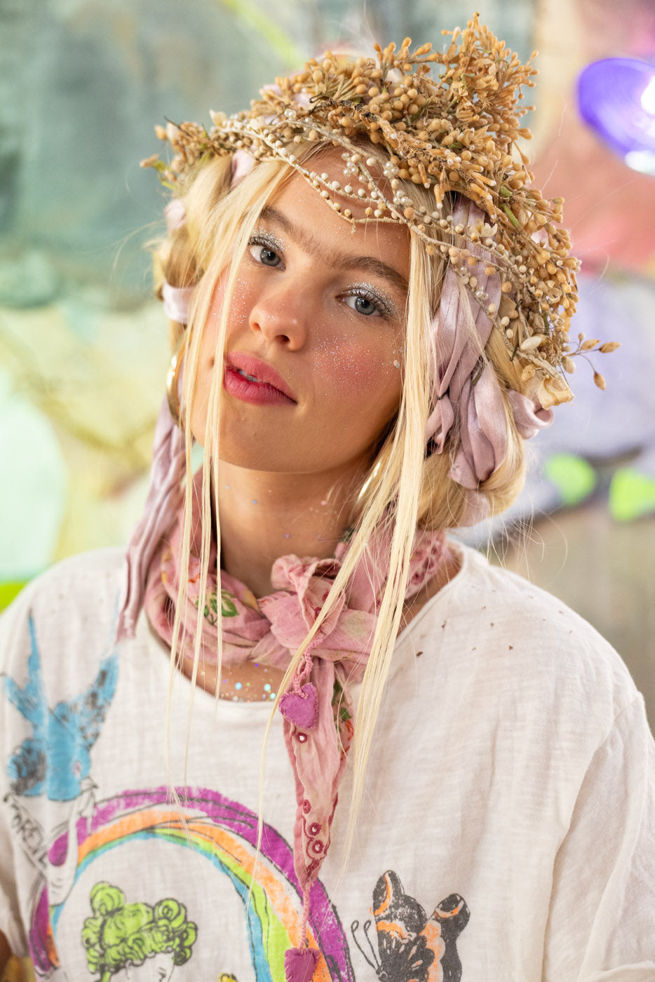Person with floral headpiece and colorful rainbow t-shirt in a natural setting