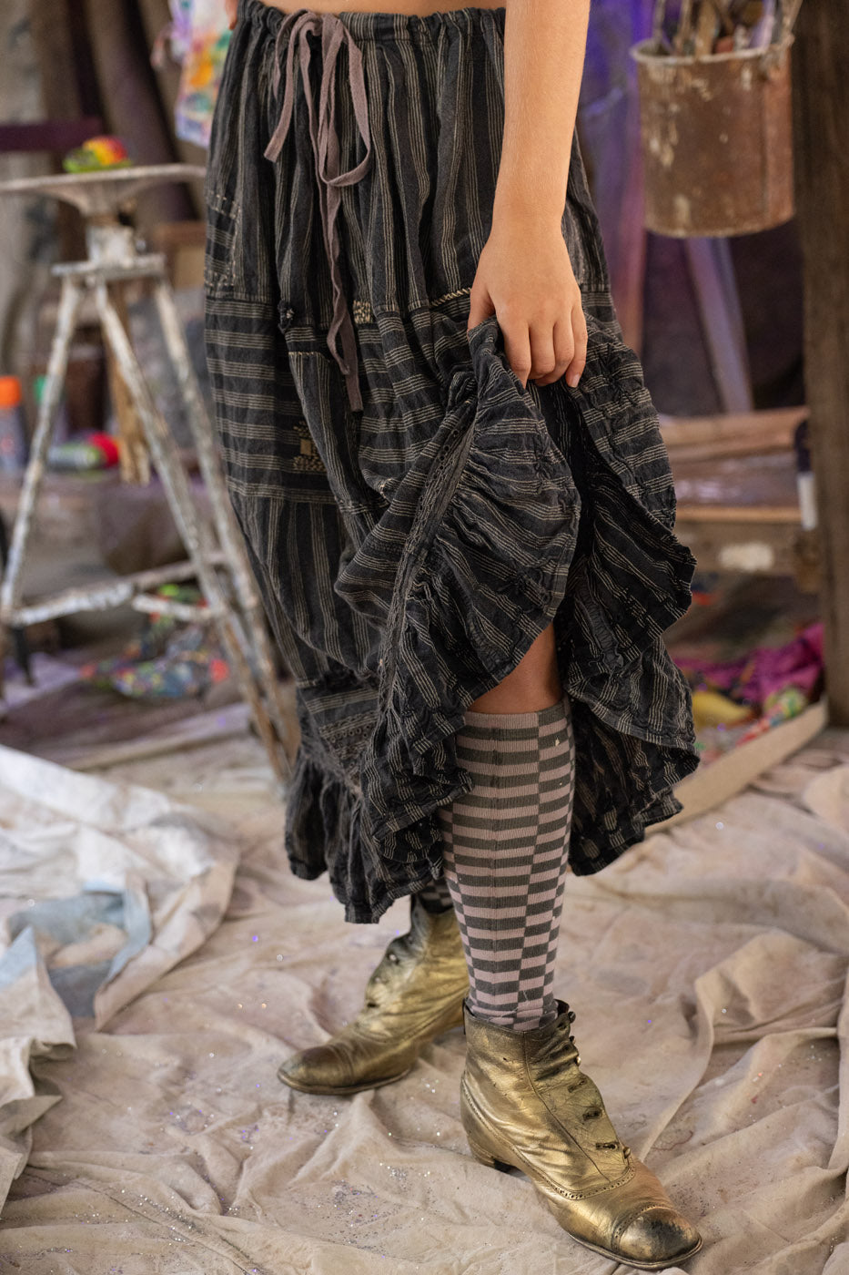Person wearing a long, gray skirt with striped socks and gold shoes in an indoor setting.