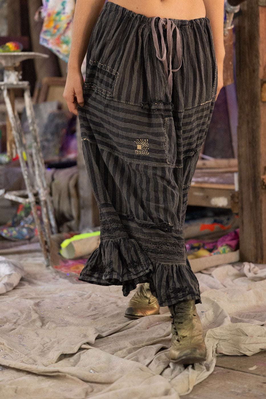 Person wearing a long, gray skirt with striped socks and gold shoes in an indoor setting.