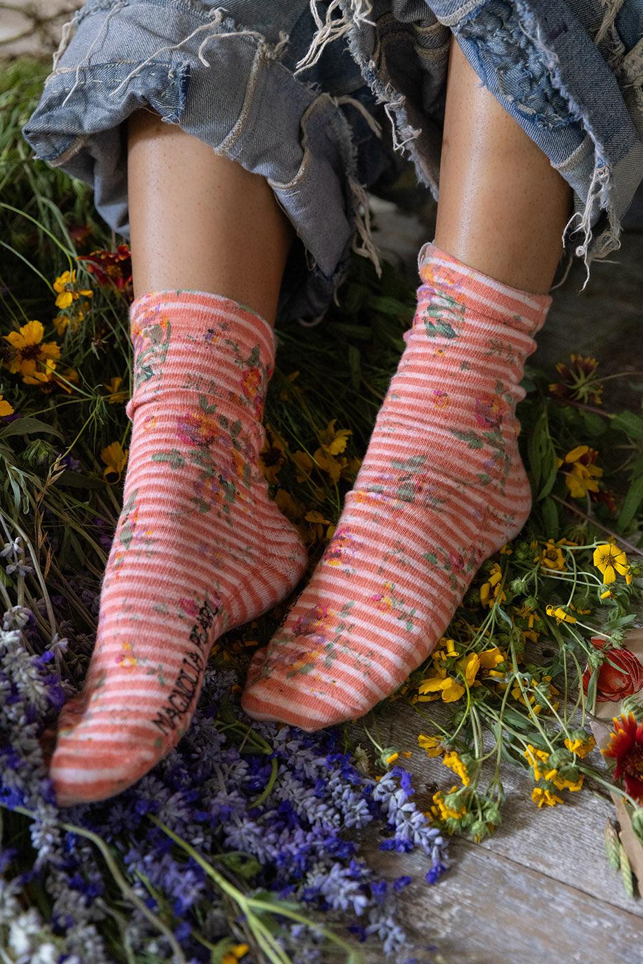 Magnolia Pearl artisan floral striped socks with whimsical vintage style, worn with ripped jeans amid wildflowers