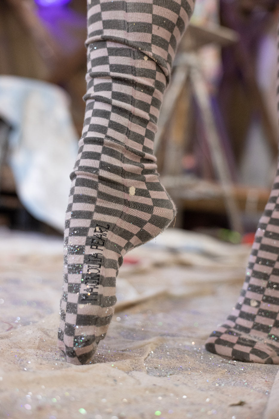 Checkered socks worn on a glittery surface with a blurred background