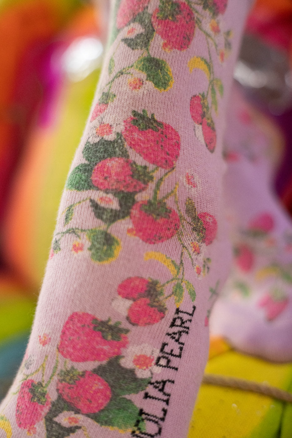 Pink socks with strawberry pattern and 'Magnolia Pearl' branding on a colorful background