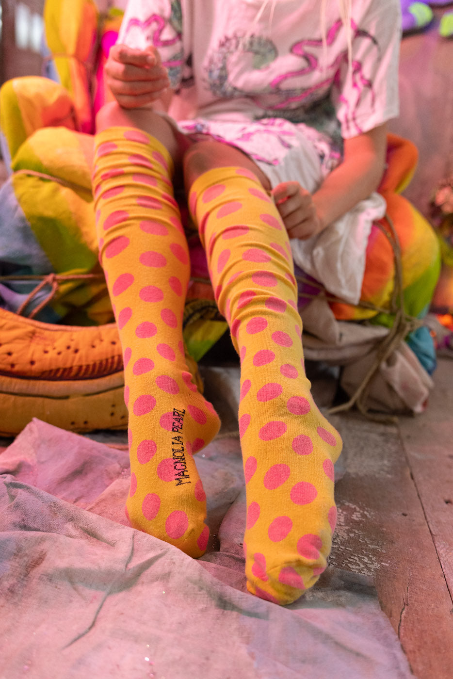 Person wearing bright yellow socks with pink polka dots sitting on a colorful chair.