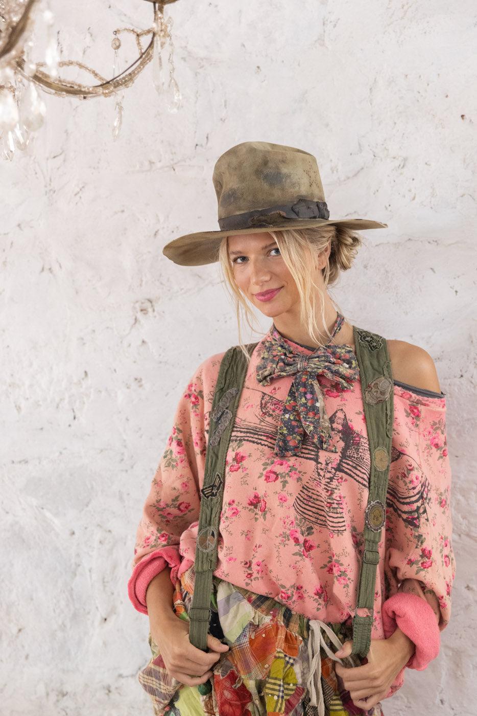 Magnolia Pearl artisan clothing model in floral pink sweater, patchwork skirt, vintage suspenders, and wide hat