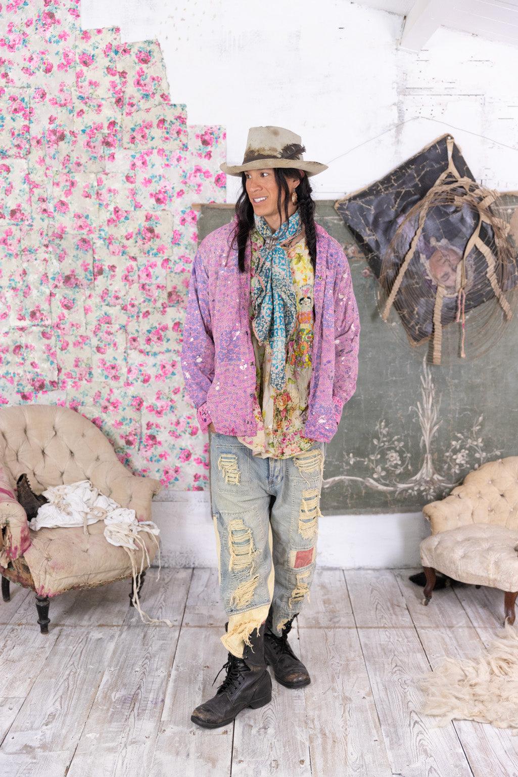 Person wearing Magnolia Pearl artisan clothing with whimsical pink jacket, vintage scarf, distressed jeans, and cowboy hat in a floral, shabby chic room