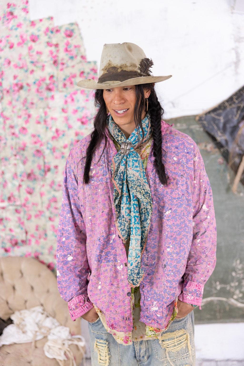 Person wearing Magnolia Pearl artisan clothing with whimsical pink jacket, vintage scarf, distressed jeans, and cowboy hat in a floral, shabby chic room