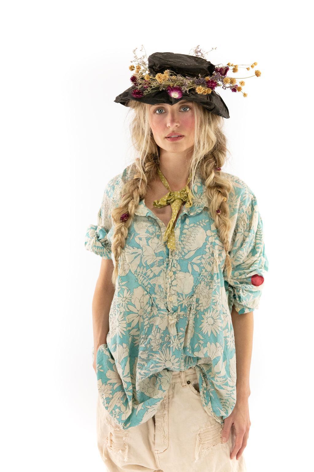 Woman in Magnolia Pearl artisan floral blouse, whimsical vintage hat with dried flowers, blonde braids