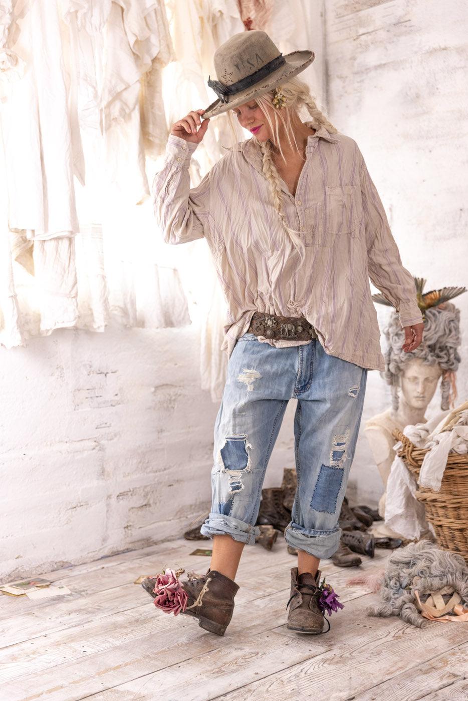 Woman in Magnolia Pearl artisan vintage shirt, hat, and jeans, sitting on distressed bench in whimsical rustic setting