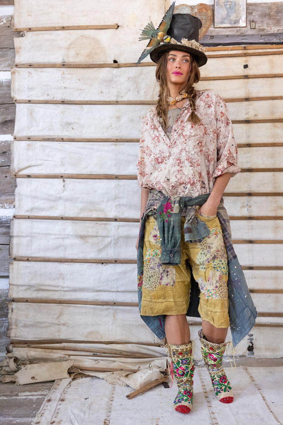 Woman in Magnolia Pearl artisan clothing, floral patchwork shorts, vintage hat with bird, whimsical style