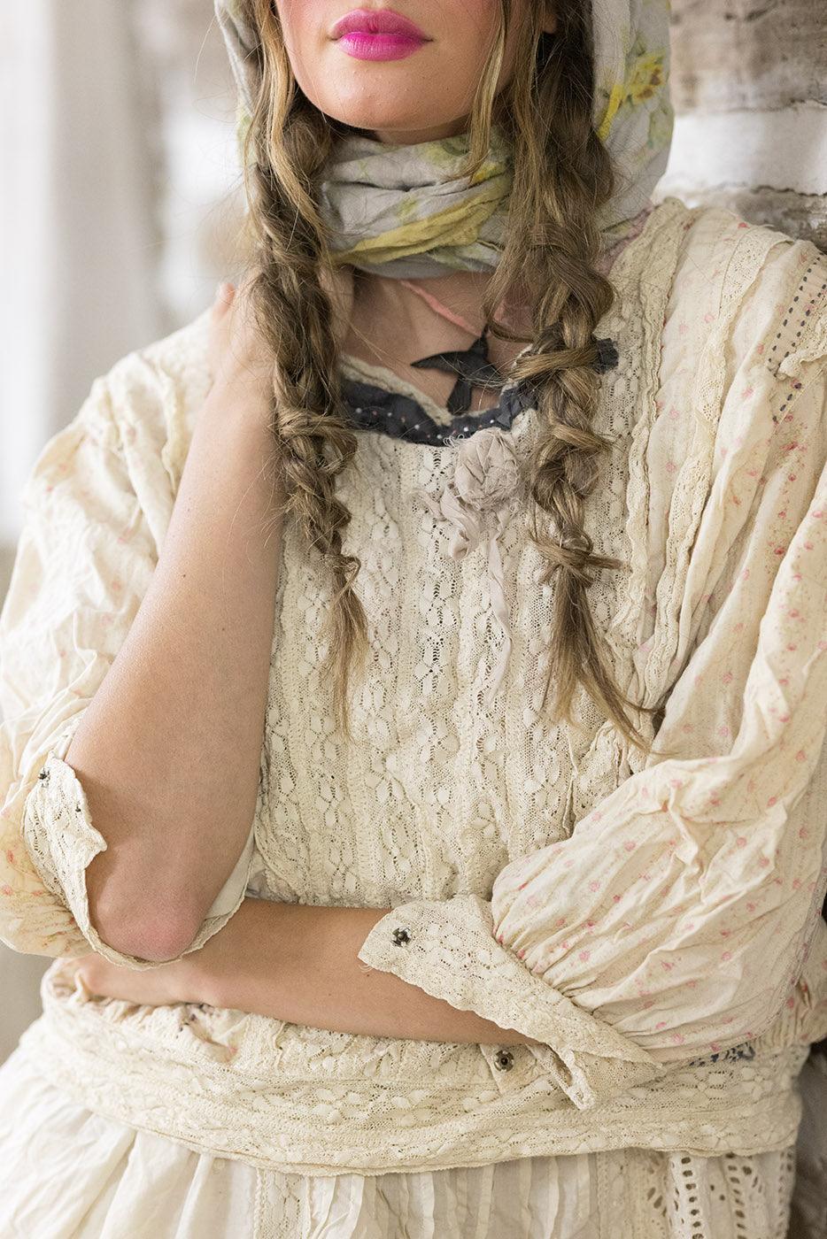Woman in Magnolia Pearl artisan vintage lace dress, whimsical smiley cap, rustic wood backdrop