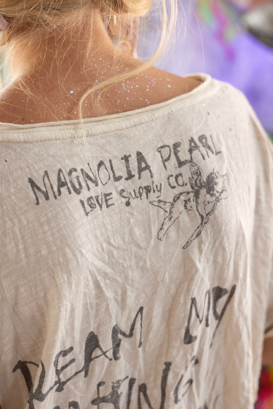 White t-shirt with text and cherub graphics, featuring 'Magnolia Pearl Love Supply Co.'