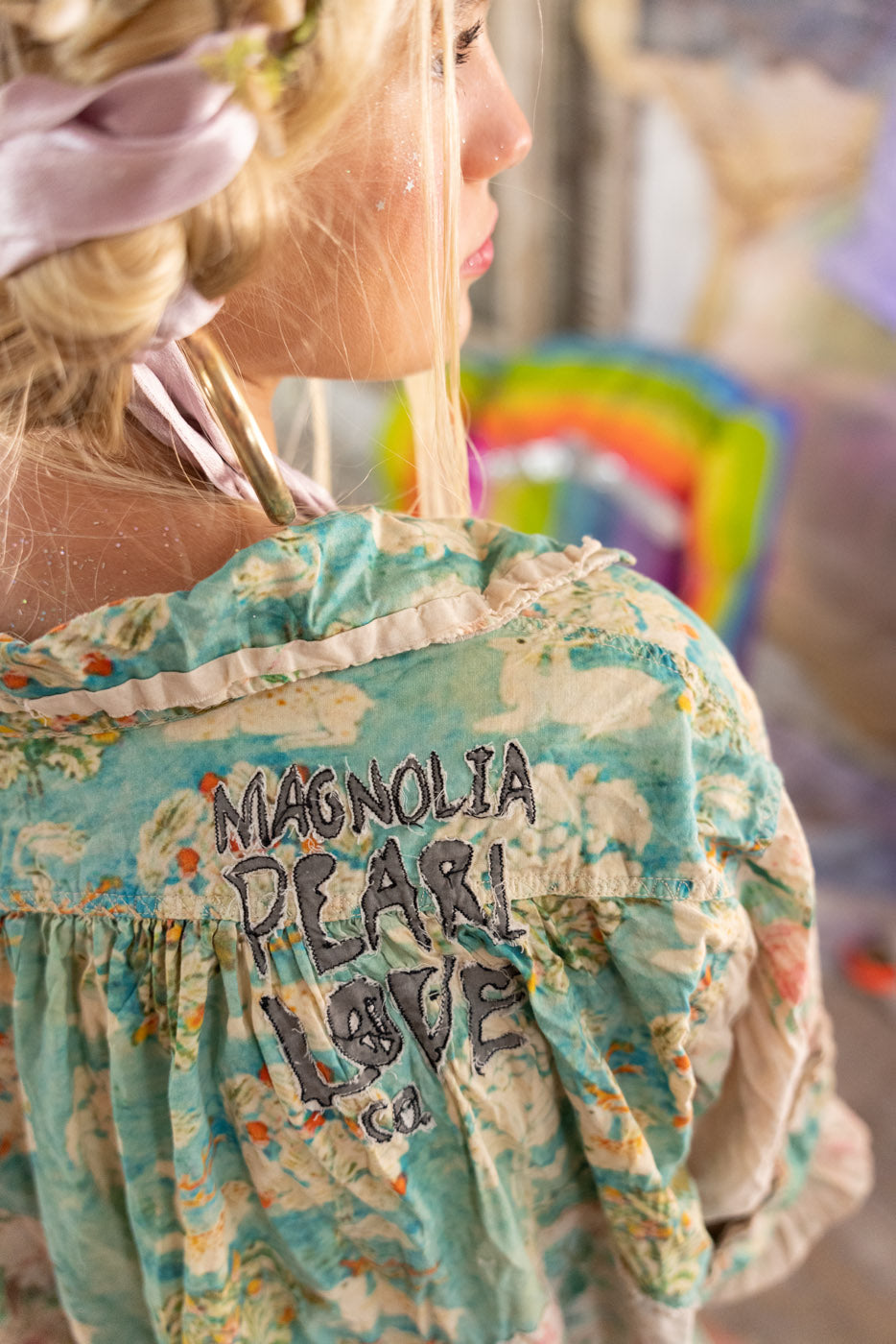 Woman wearing a floral blouse with 'Magnolia pearl Love' text, blurred background