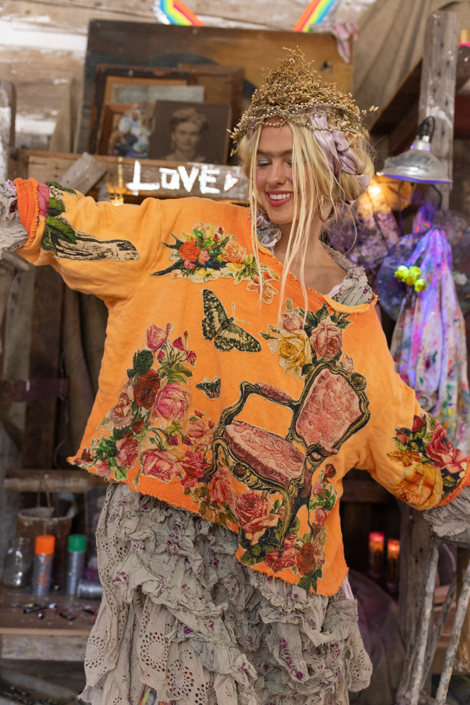 Person wearing a bright orange crew neck sweatshirt with floral, vintage, and heart designs in a casual setting.