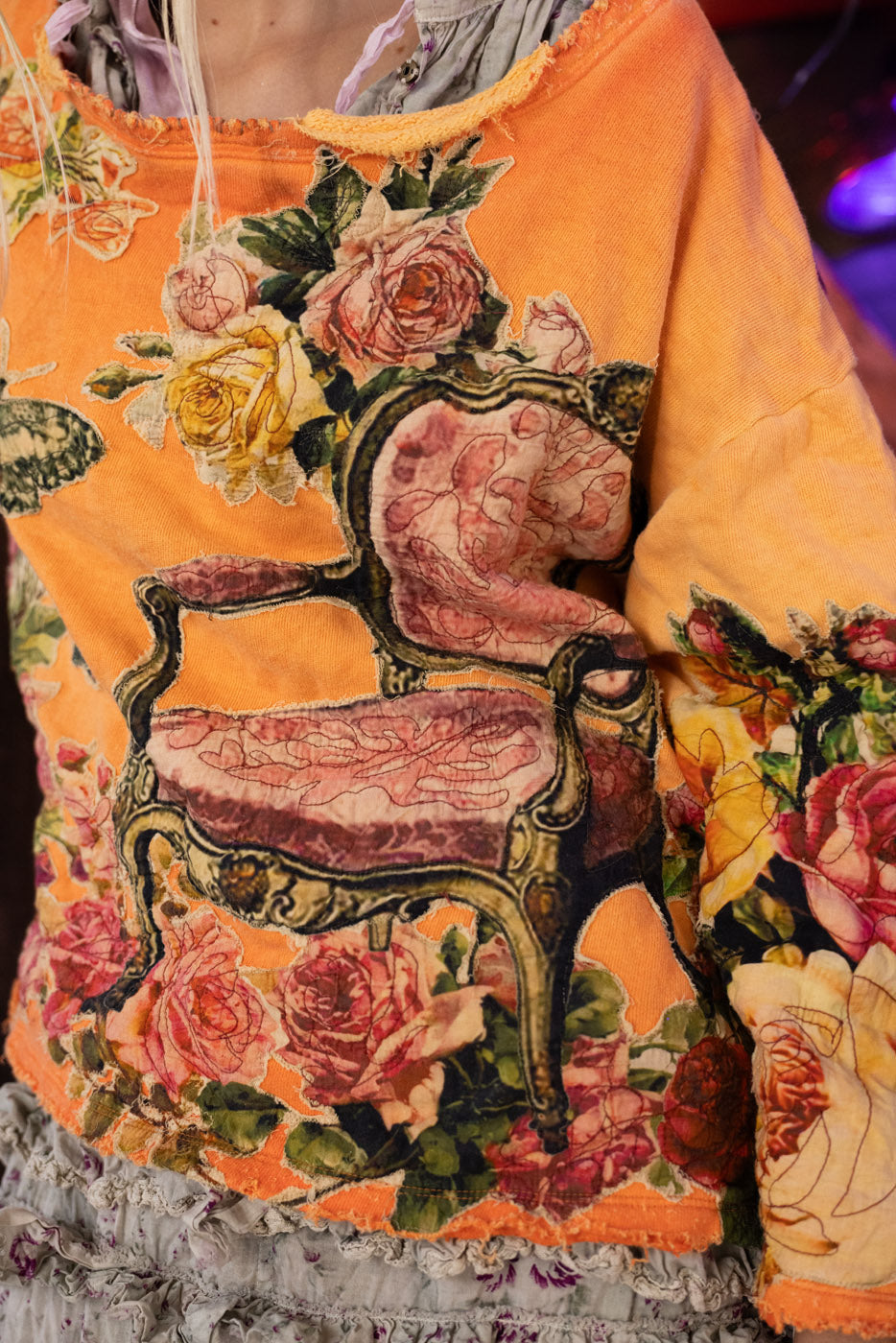 Close-up of a colorful crew neck sweatshirt with floral and chair design on an orange background