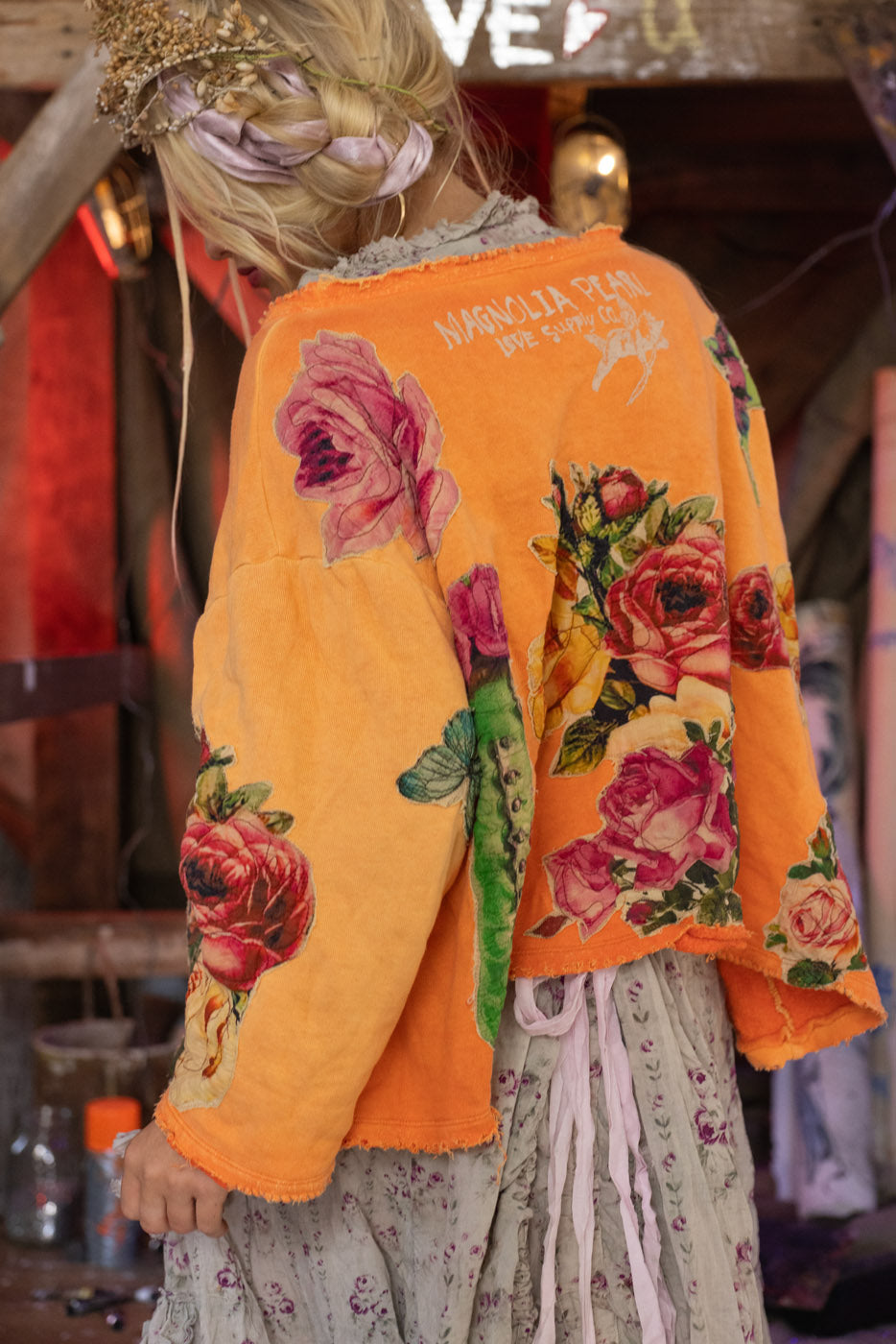 Model wearing an orange floral-patterned sweatshirrt with a blurred background.