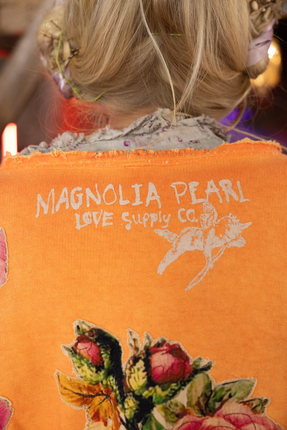 Orange sweatshirt with 'Magnolia Pearl Love Supply Co.' branding and floral design.