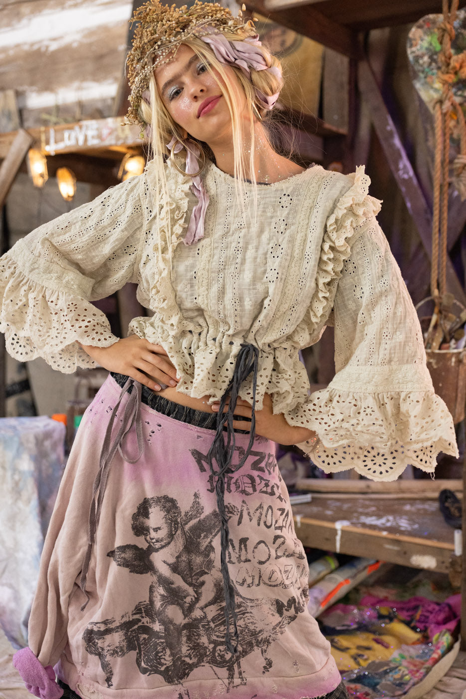 Person wearing a bohemian-style outfit with lace top and printed pants in a rustic setting.