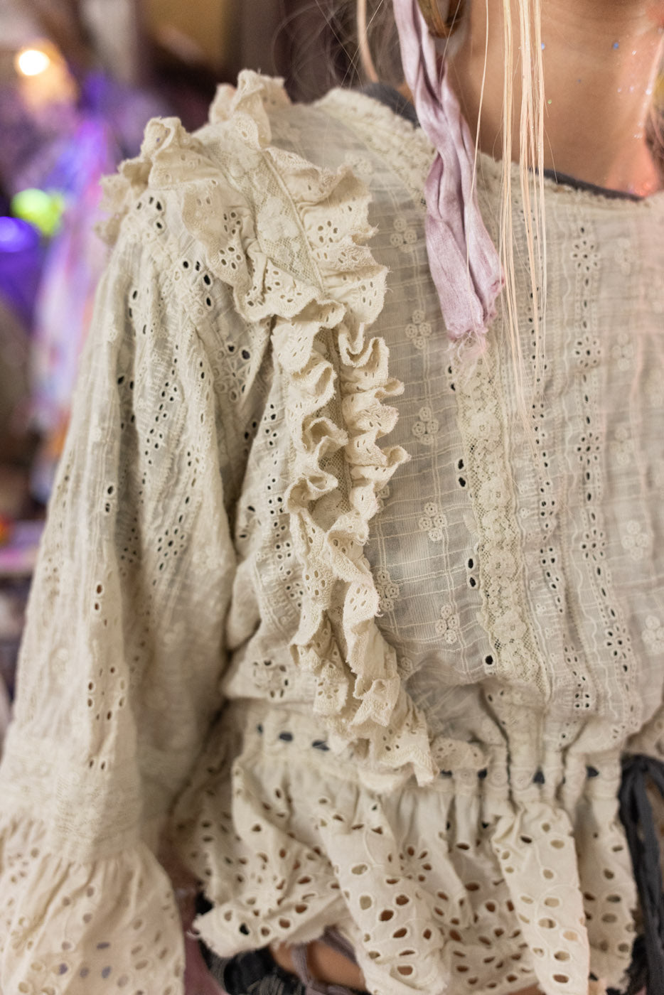 Close-up of a person wearing a beige lace blouse with ruffled details.