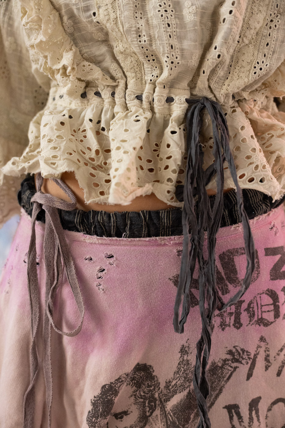 Close-up of a person wearing a beige lace top with grey detailing to sinch waist.