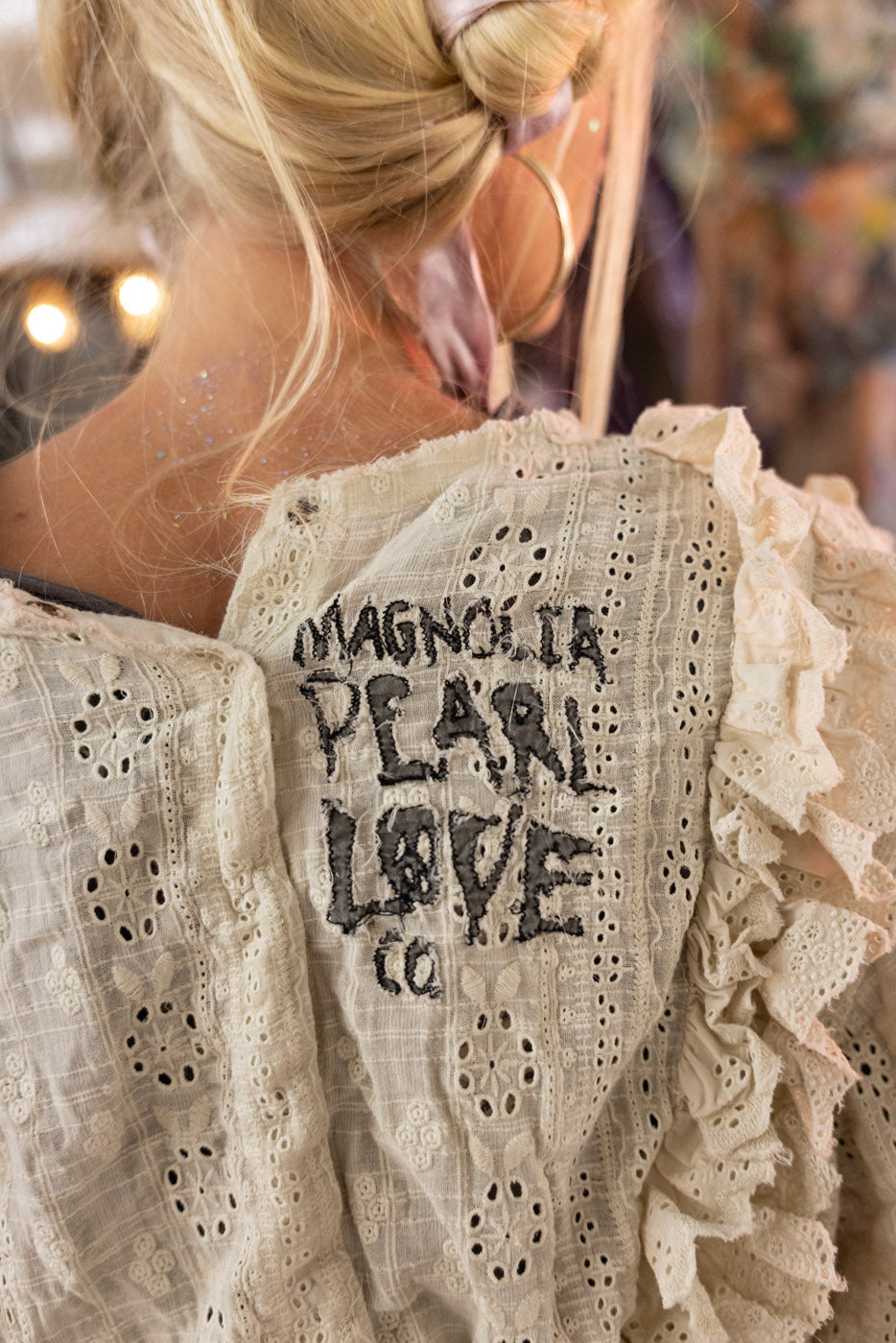 Close-up of a lace garment with 'Magnolia Pearl Love Co.' embroidery.